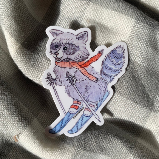 Watercolor drawing on a sticker of a raccoon wearing skis on top of a plaid flannel background