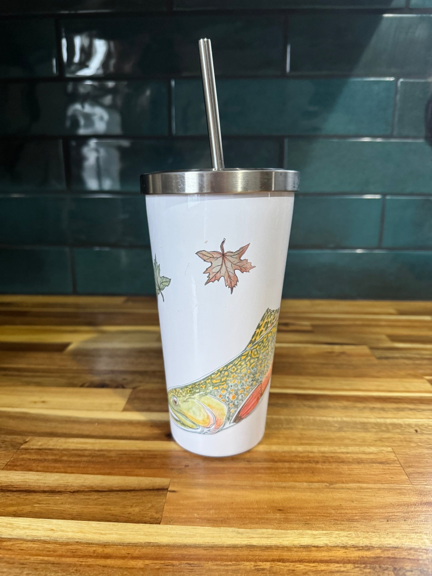 Tumbler with a fish design on a wooden surface with a teal tiled wall in the background