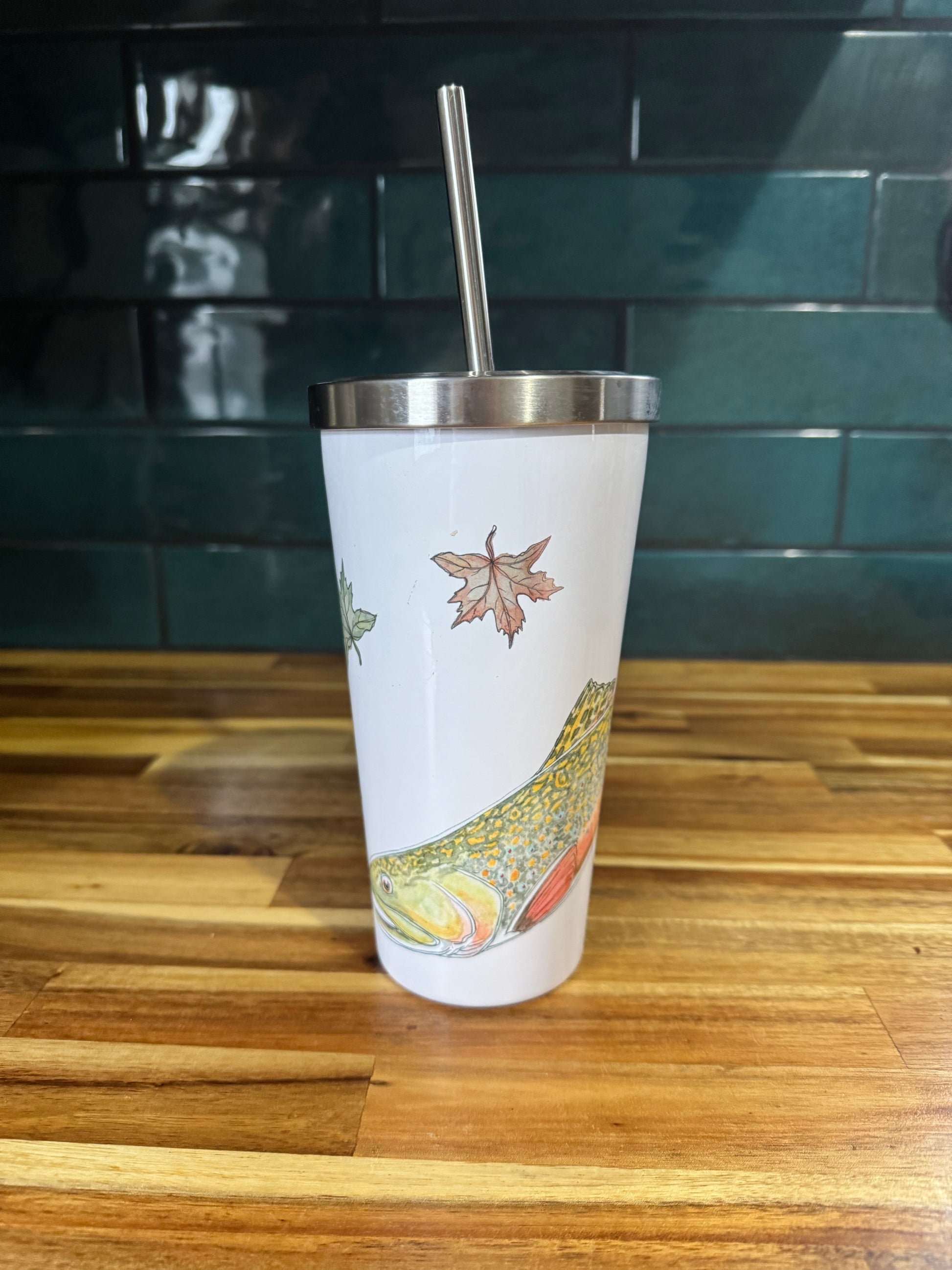 Tumbler with a fish design on a wooden surface with a teal tiled wall in the background