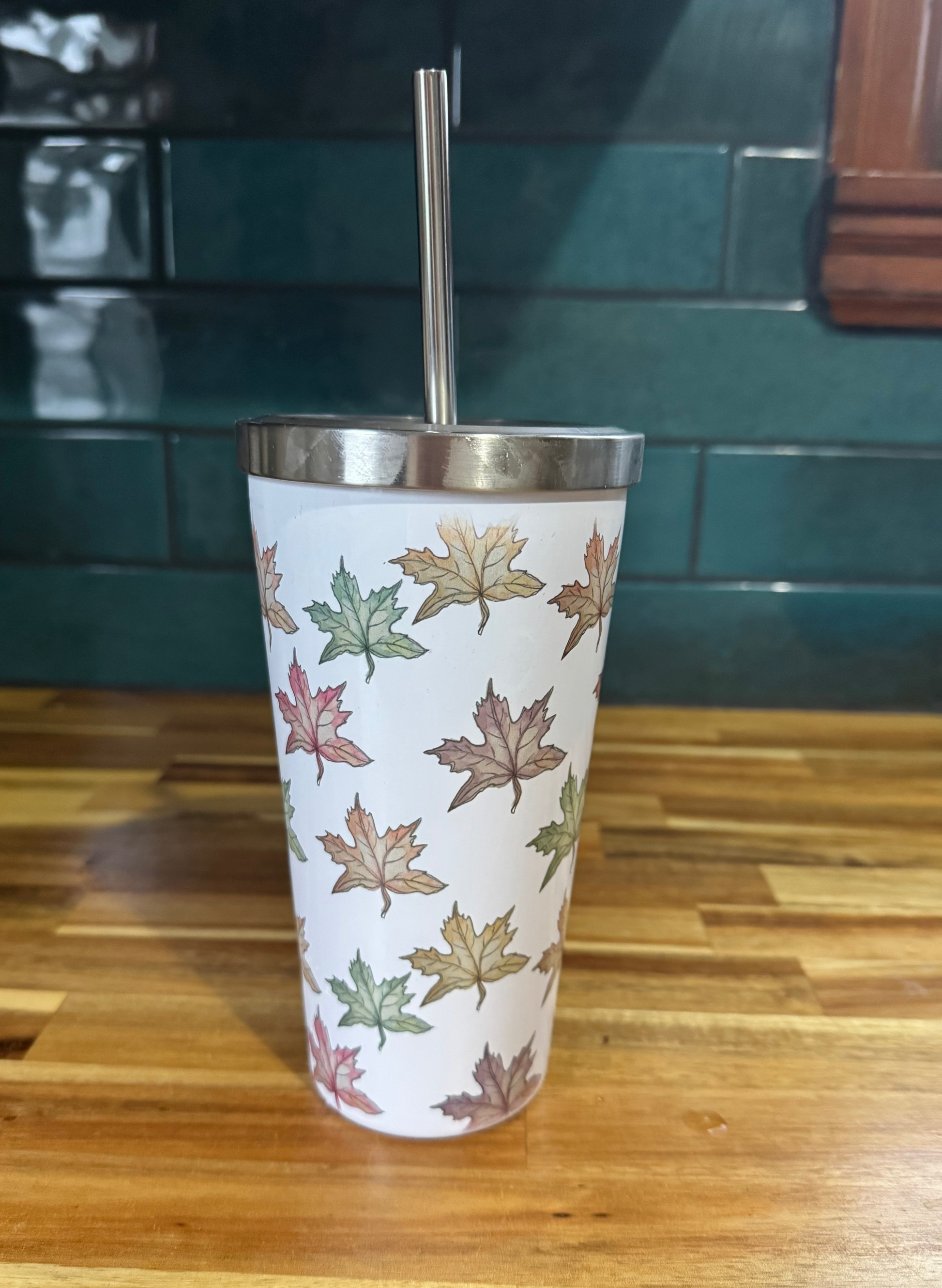 Tumbler with leaf pattern on a wooden surface with a teal tiled wall in the background