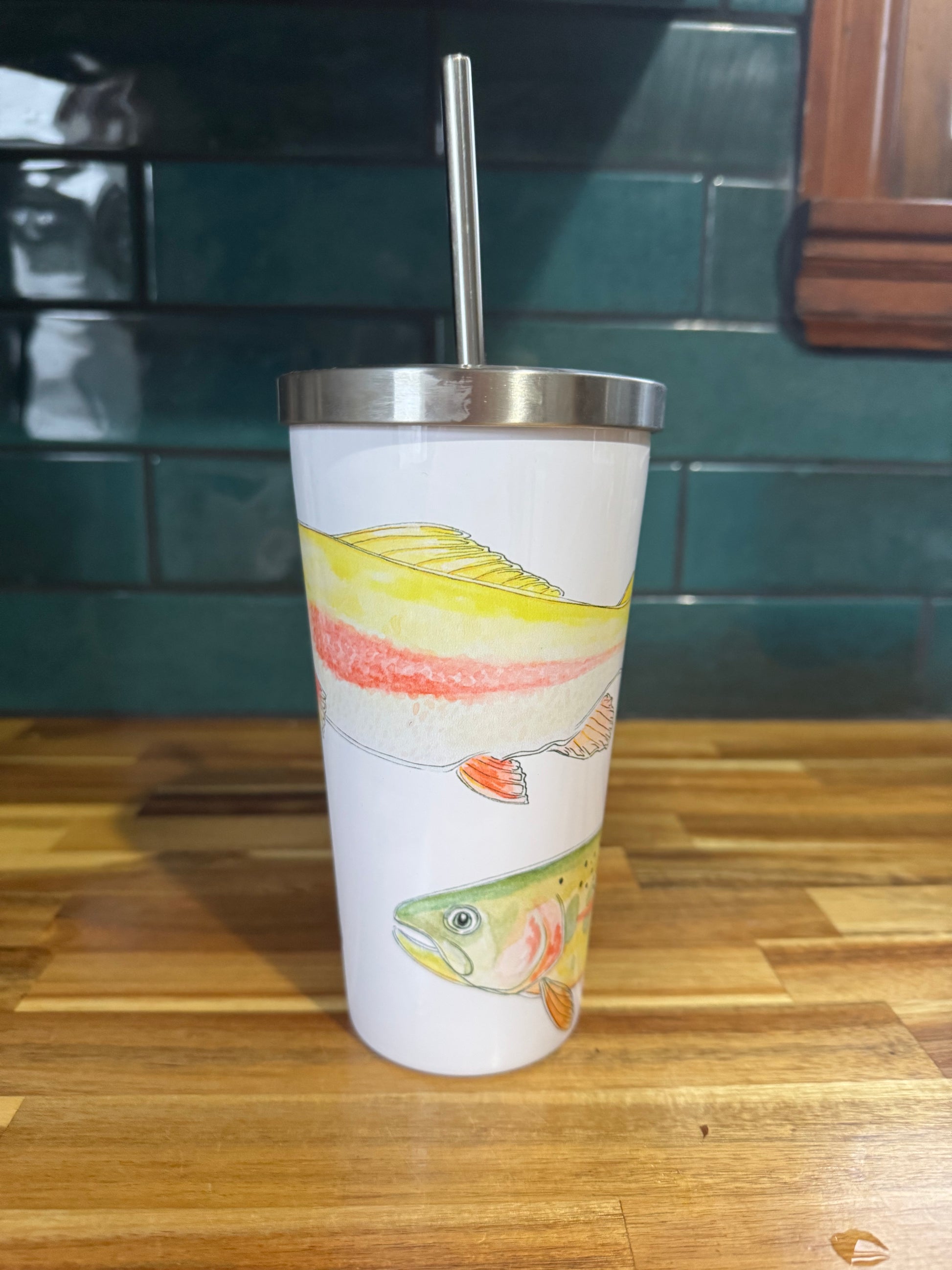 Tumbler with fish design on a wooden surface and green tiled wall background