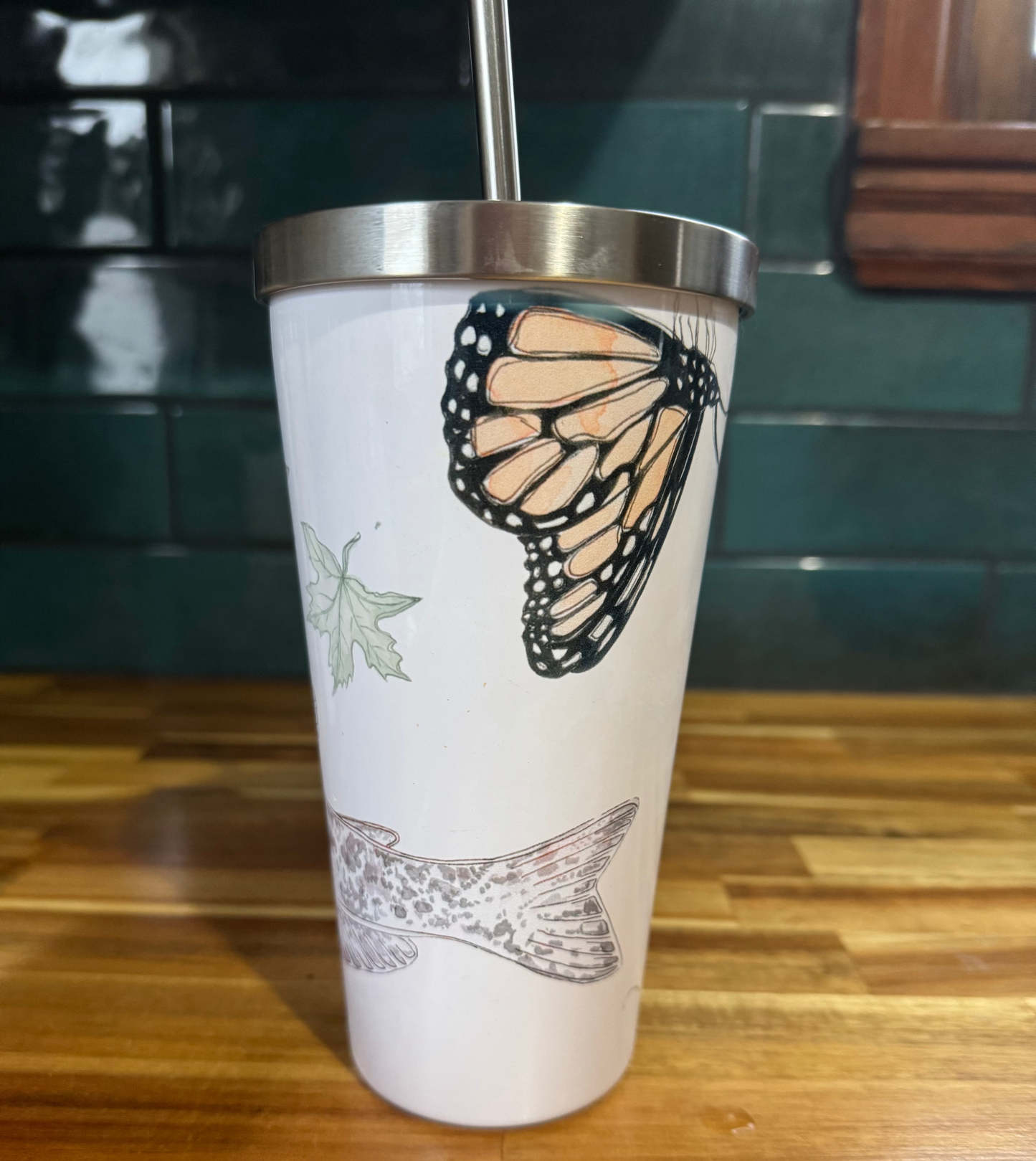 Tumbler with butterfly design on a wooden surface and tiled wall background