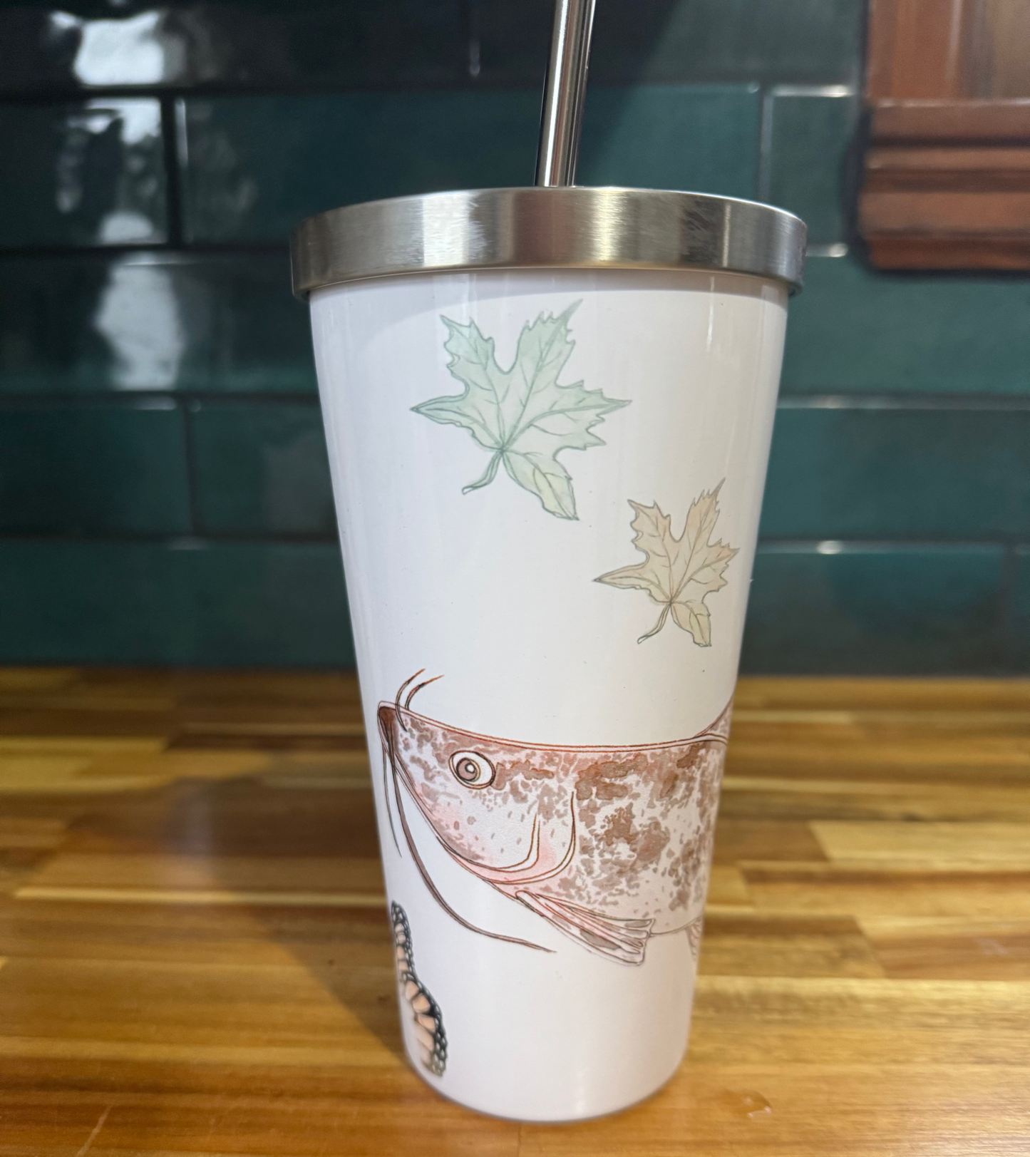 Tumbler with fish and leaf design on a wooden surface
