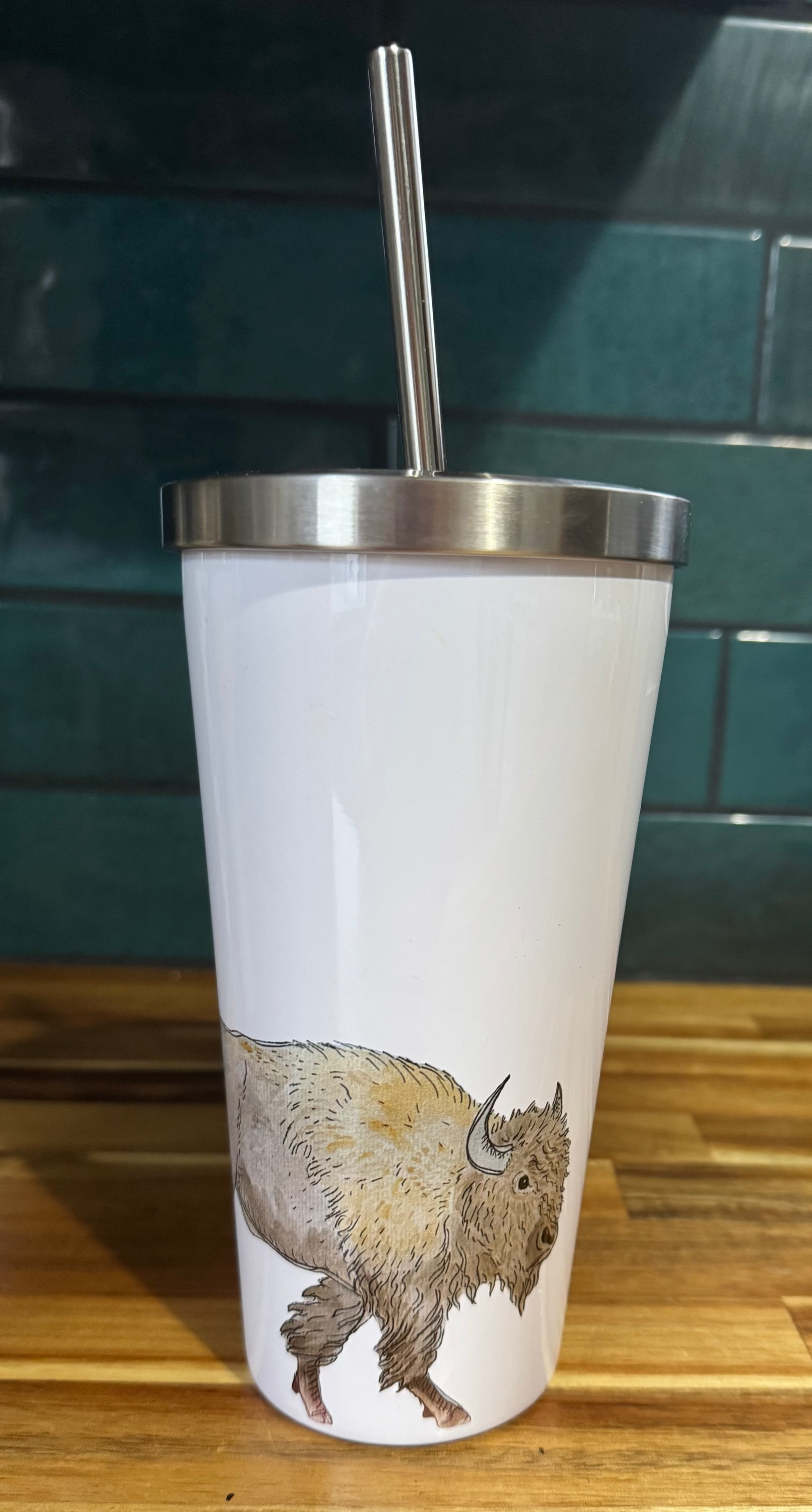 Tumbler with a bison design on a wooden surface with a green tiled wall in the background